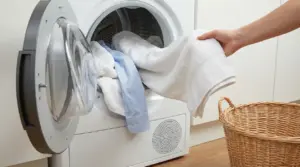 Una mano sta estraendo indumenti asciutti da un'asciugatrice accanto a un cesto di vimini.