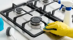 Pulizia di un fornello a gas con spugna e guanto in lattice giallo