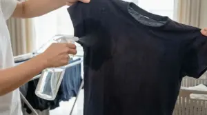 Persona spruzza una soluzione su una maglia nera, concentrandosi sull’area delle ascelle per eliminare l’odore di sudore