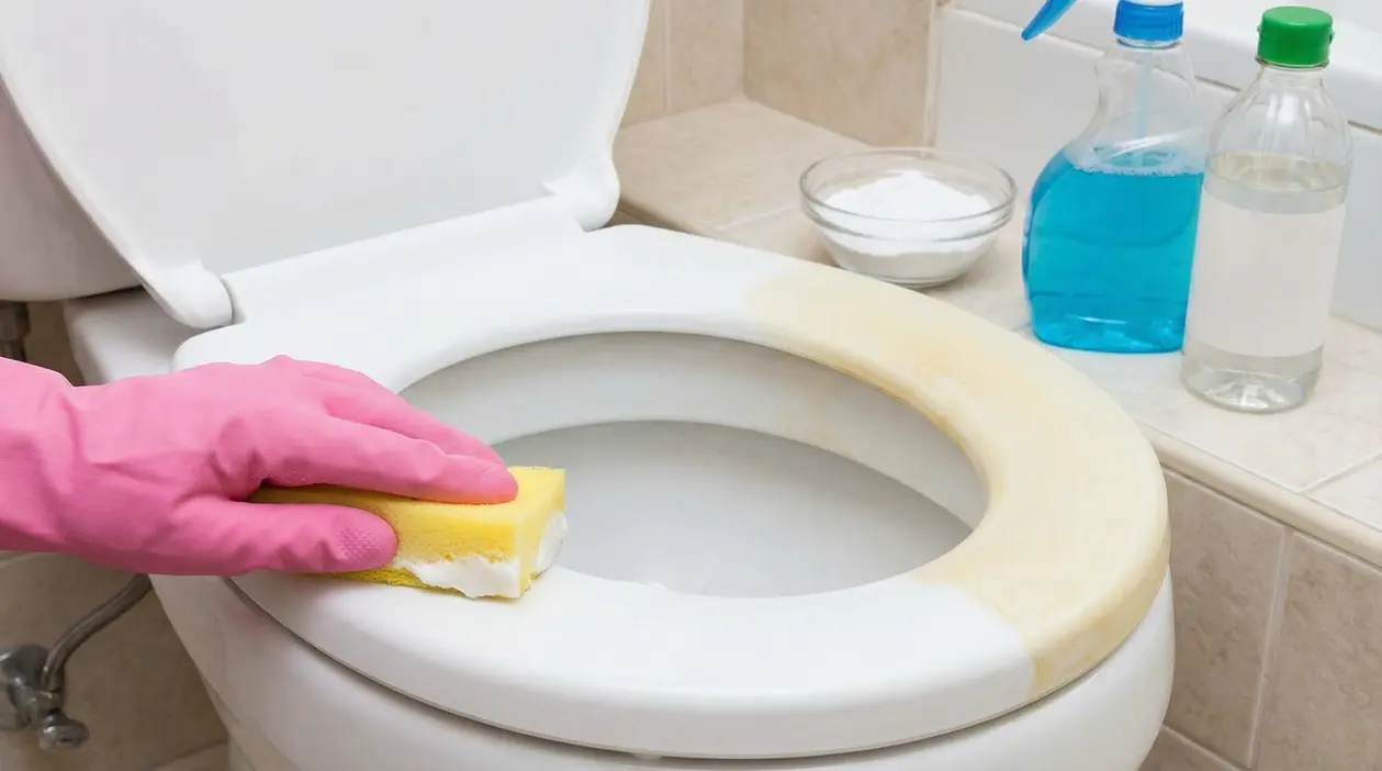 Persona pulisce la plastica ingiallita del WC con una spugna e guanti rosa
