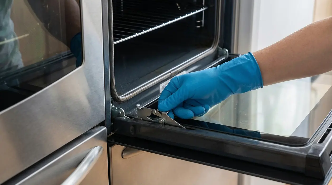 Mano con guanto blu che regola una manopola sullo sportello di un forno aperto