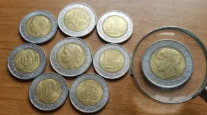 Varie monete italiane da 500 lire bimetalliche disposte su un tavolo di legno con una lente d'ingrandimento