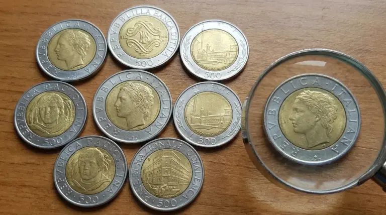 Varie monete italiane da 500 lire bimetalliche disposte su un tavolo di legno con una lente d'ingrandimento