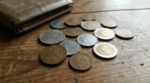 Vecchie monete italiane sparse su un tavolo di legno accanto a un portafoglio in pelle