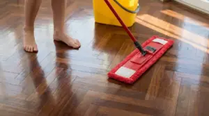 Persona che lava un parquet lucido con mop rosso e secchio giallo in una stanza luminosa